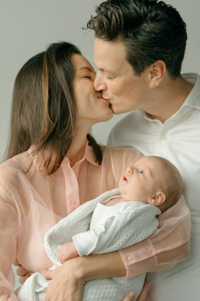 new parents kiss holding their baby between them