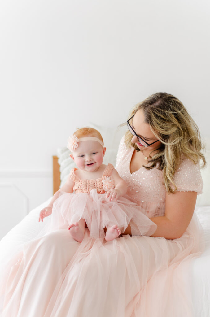 baby girl wearing an ethereal pink dress smiles on mom's lap