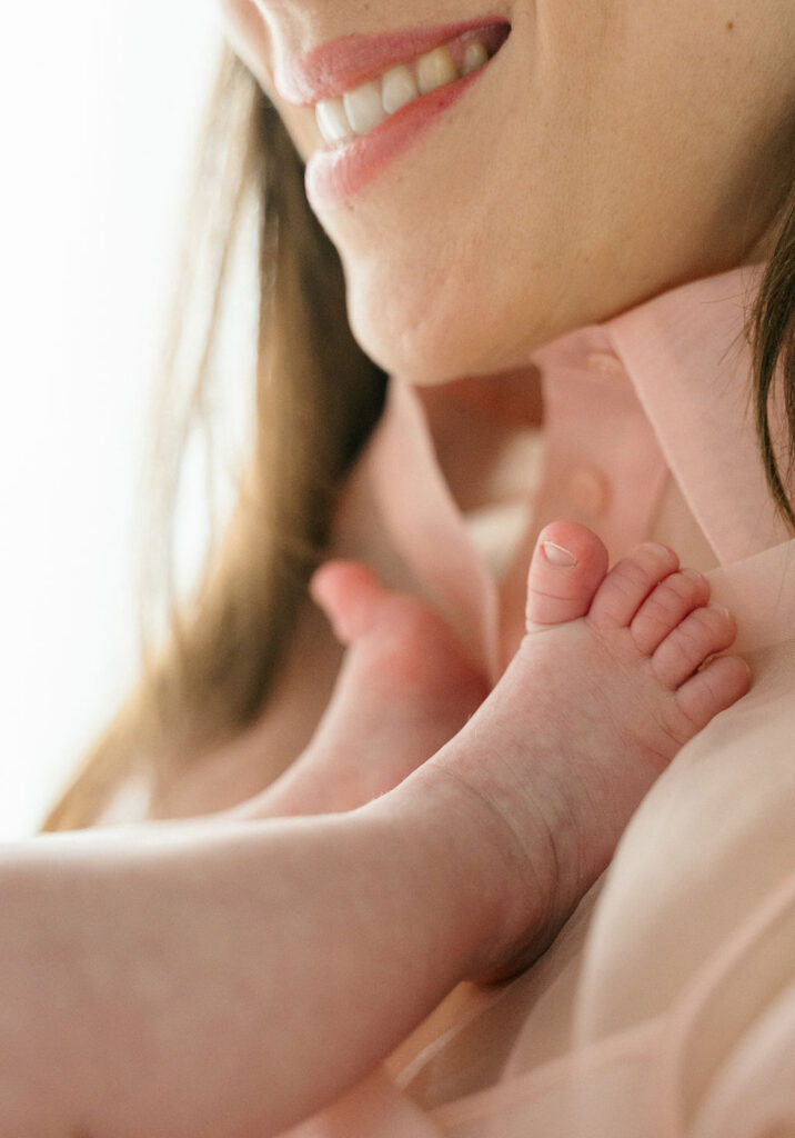 close up of newborn baby feet on mom's chest with her smiling down at them
