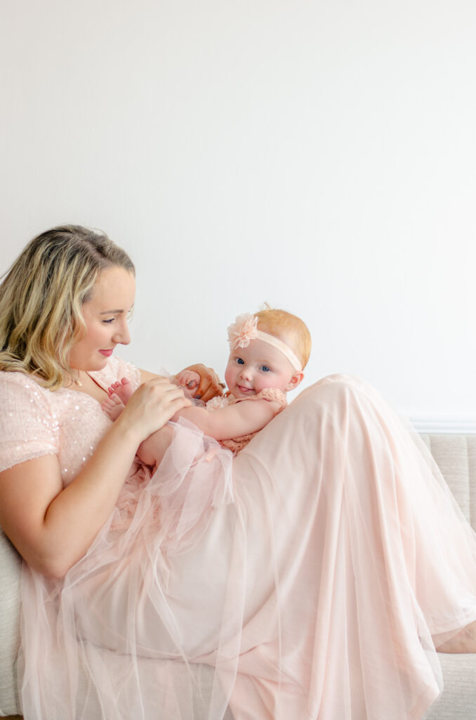 baby in roze jurk op moeders schoot in een witte fotostudio