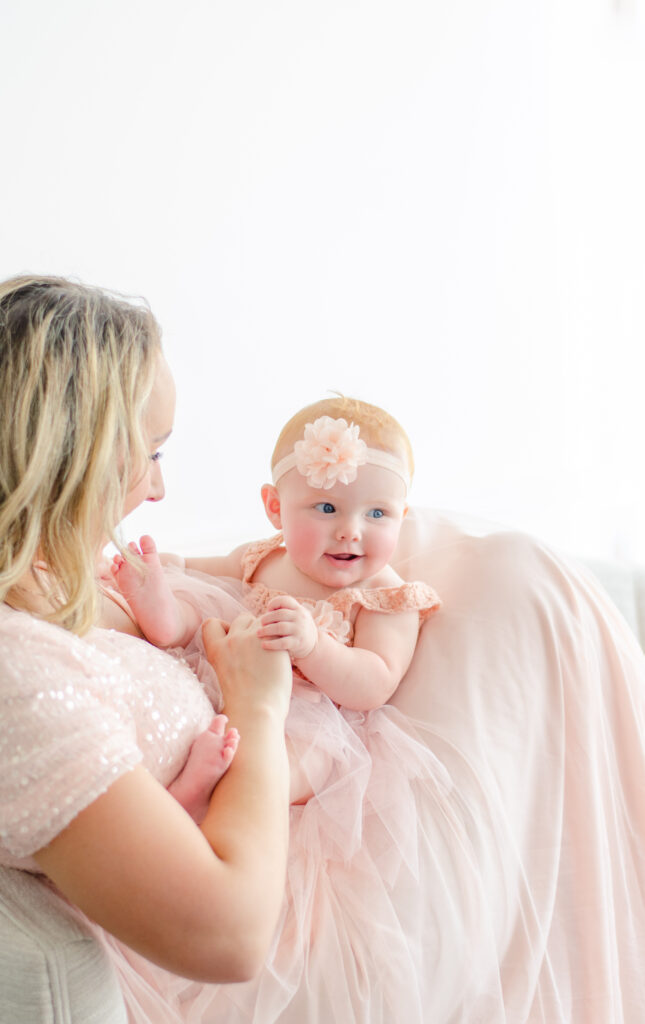 baby in roze jurk op moeders schoot in een witte noord holland fotostudio 