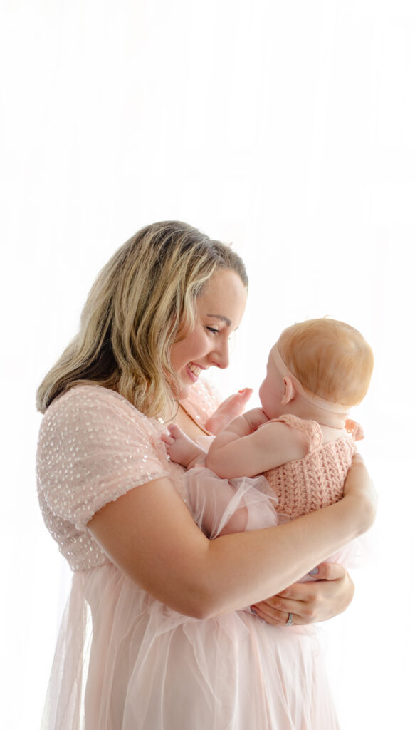 mom and baby smile at each other in an all white amsterdam photography studio