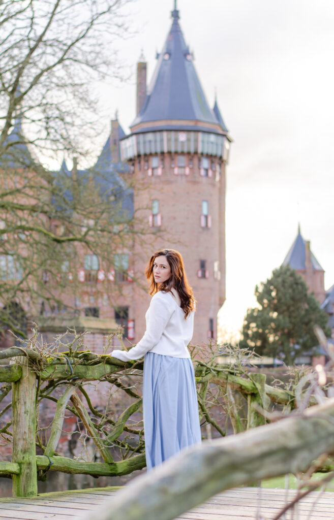 woman looks behind her standing on a fairytale bridge covered with green vines at kasteel de haar in the netherlands