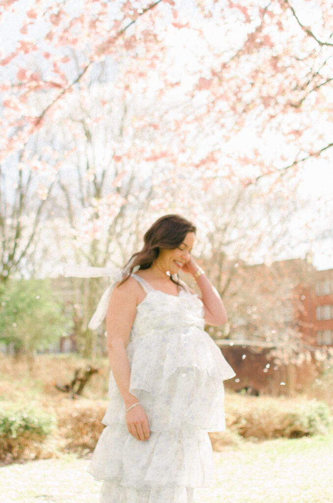 Editorial photograph of a mother-to-be in the sun under the cherry blossoms.