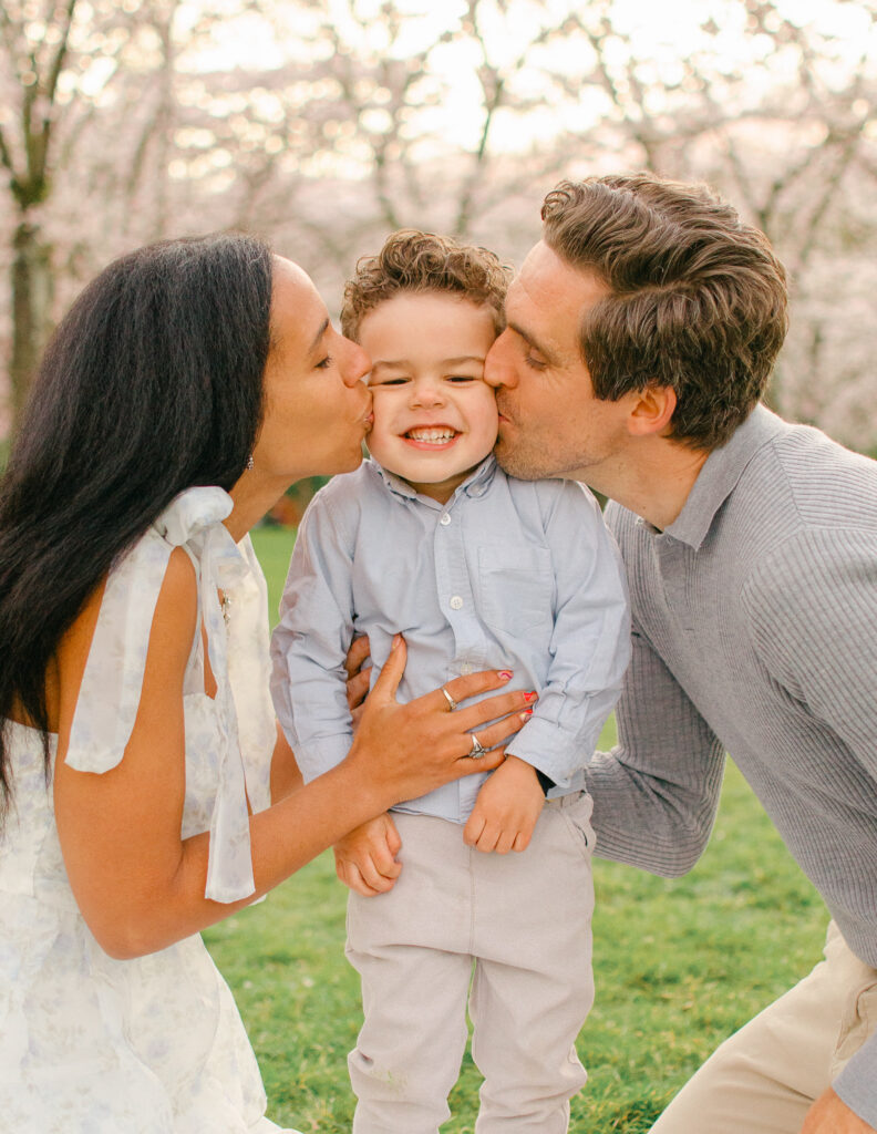 parents give their toddler son a kiss on the cheek in the bloesempark under the cherry blossoms at sunset