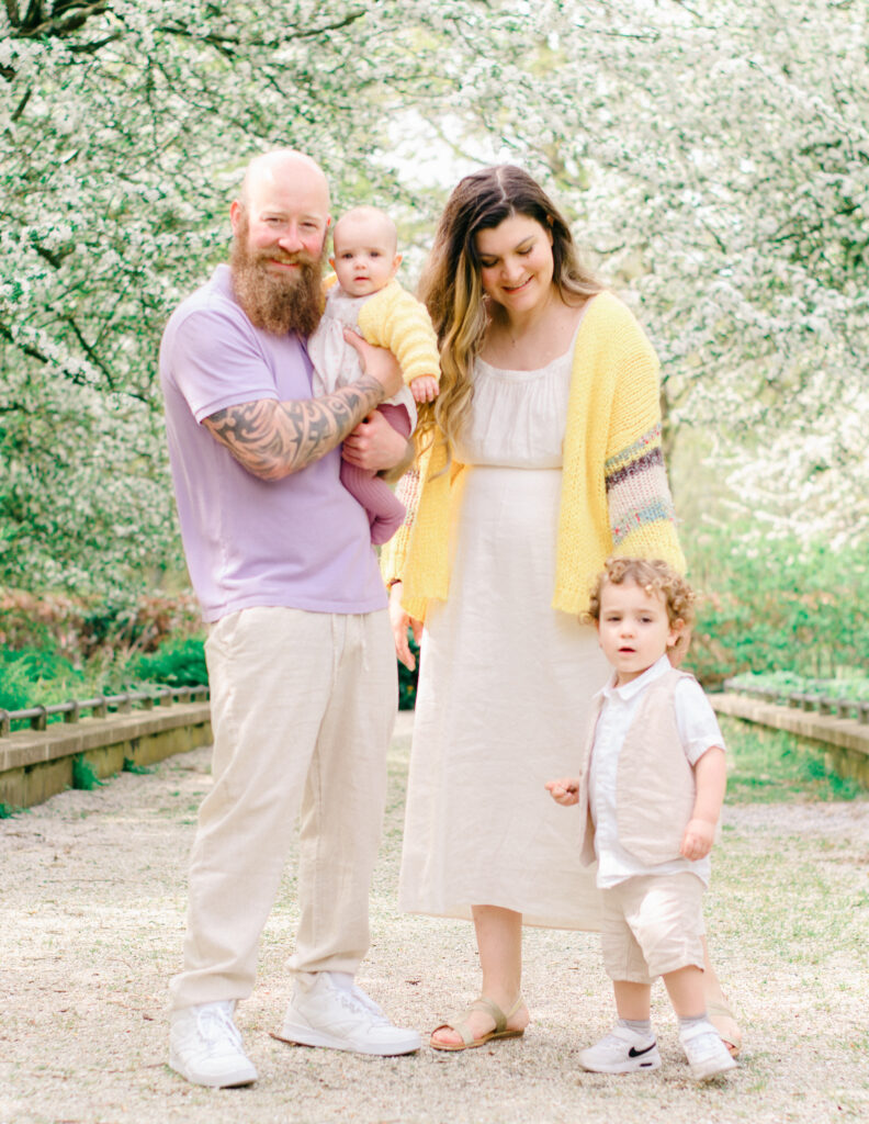 A family dressed in yellow and lavender pastels smile in a garden for their portraits.
