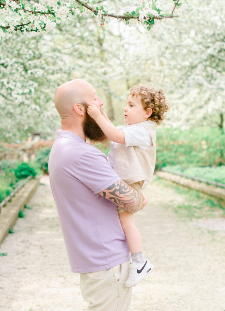 Young son grabs his father's face under the spring blossoms.