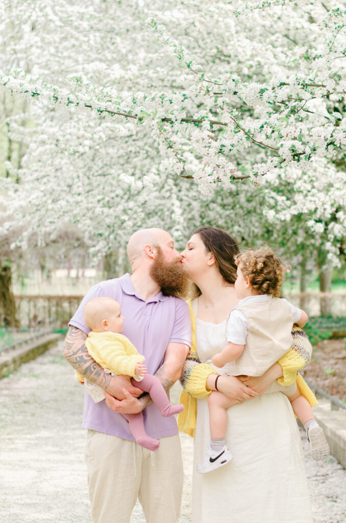 Husband and wife share a peck on the lips as they hold their two children.