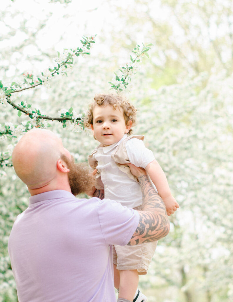 Father lifts his son up into the white almond blossoms.