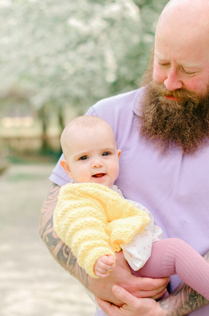 Father holds infant baby daughter in his arms in the spring.