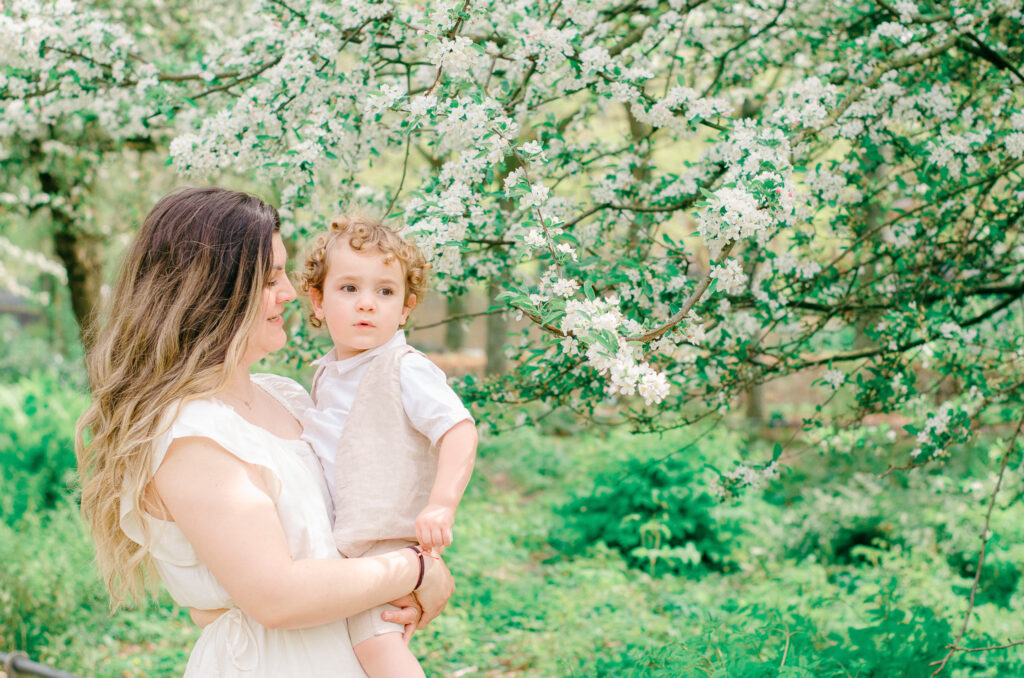 Mother lovingly looks at her young son in a garden full of spring blooms.