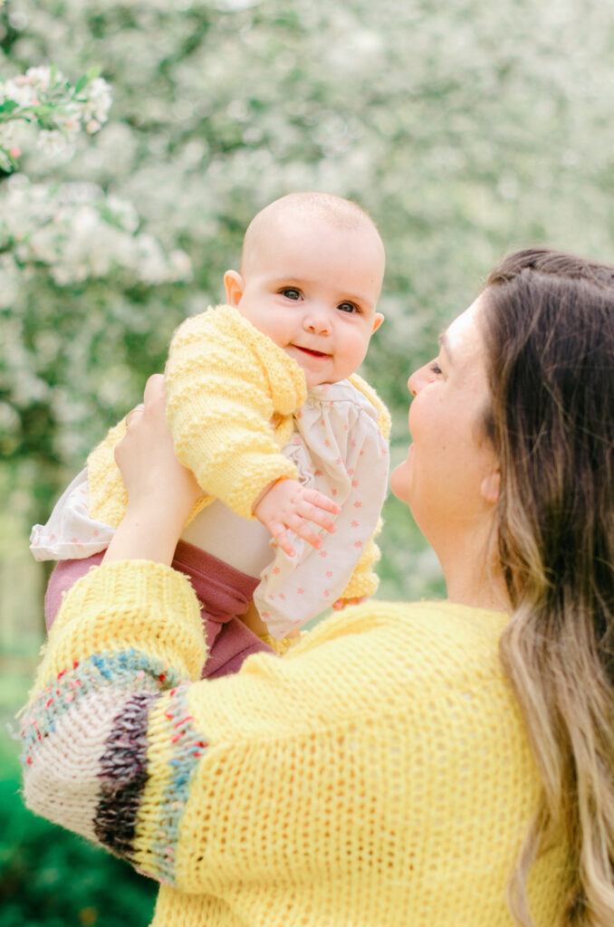 Mother and infant daughter, both in bright yellow sweaters, enjoy the park filled with spring blossoms.