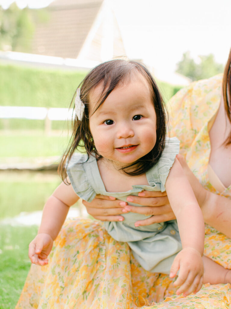 Daughter squirms in mom's lap sitting in the grass next to a canal in Giethoorn.