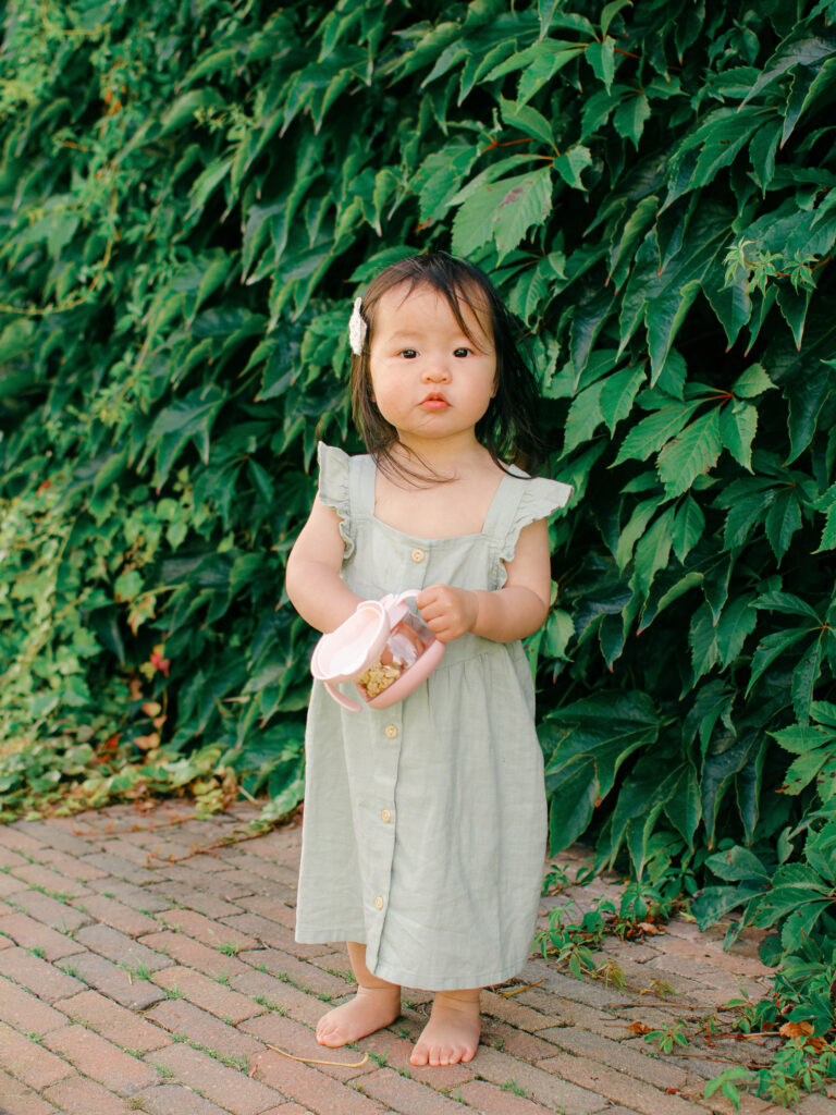 Candid photograph of toddler snacking in front of an ivy covered wall.