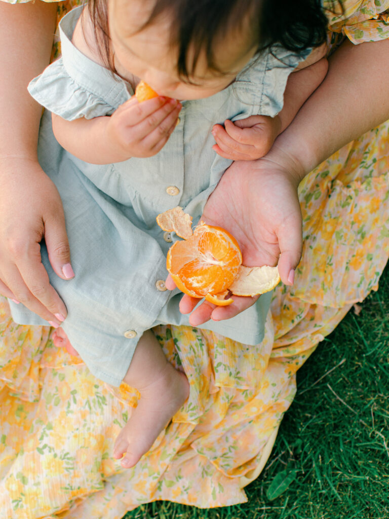Lifestyle-editorial image of mom feeding toddler oranges by the canal in Giethoorn.