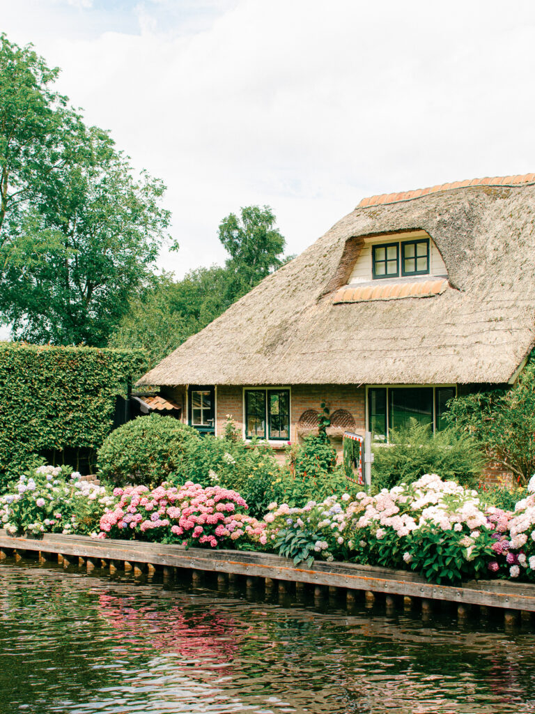 A house on the canal in Giethoorn with a garden bursting with blooms in the full sun.