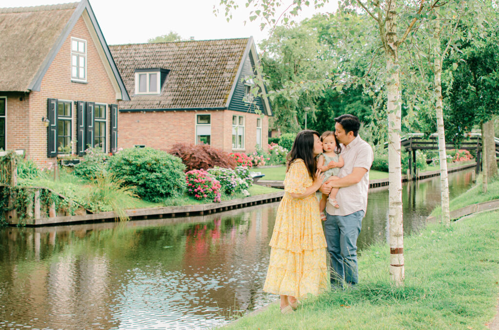 Parents give toddler daughter a kiss on the cheek by the canals.