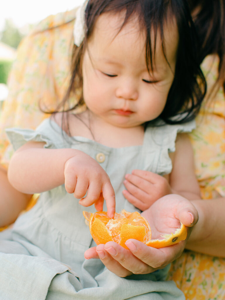Baby girl curiously inspects her orange before eating it.