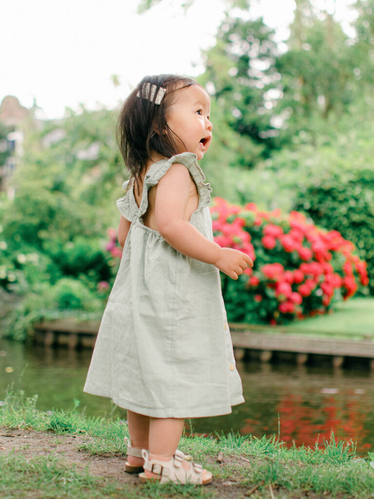 Happy baby in light sage dress stomps around on the grass by the canals.