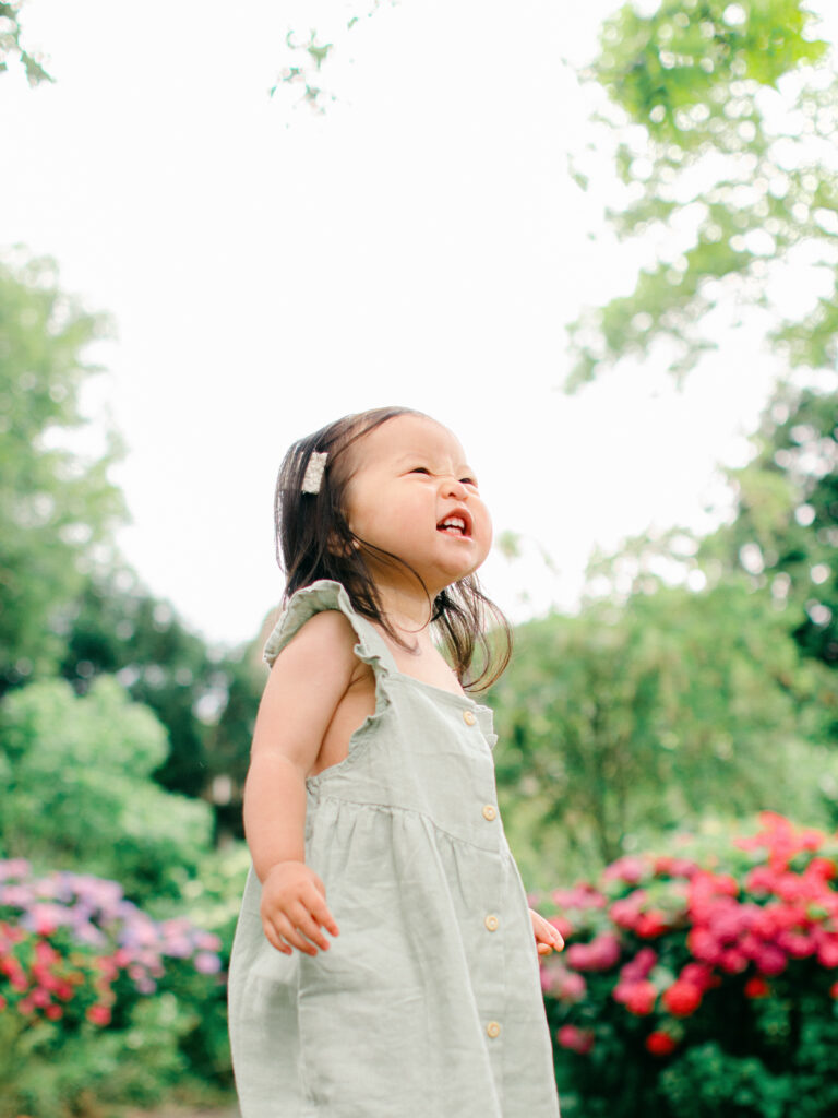 Worm's-eye-view of a toddler girl in Giethoorn, with hydrangeas behind her.