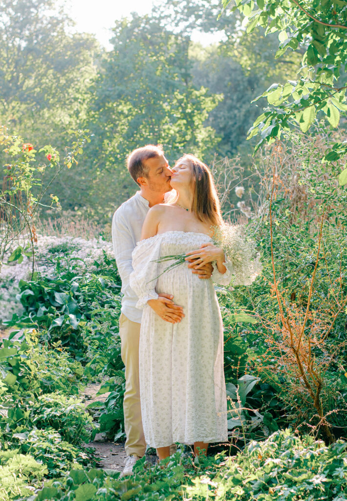 Expecting couple in pastels kiss in the Miracle Garden in Amsterdam.