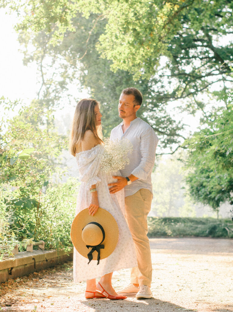 Father-to-be puts hand on wife's baby bump in a garden in the early afternoon.