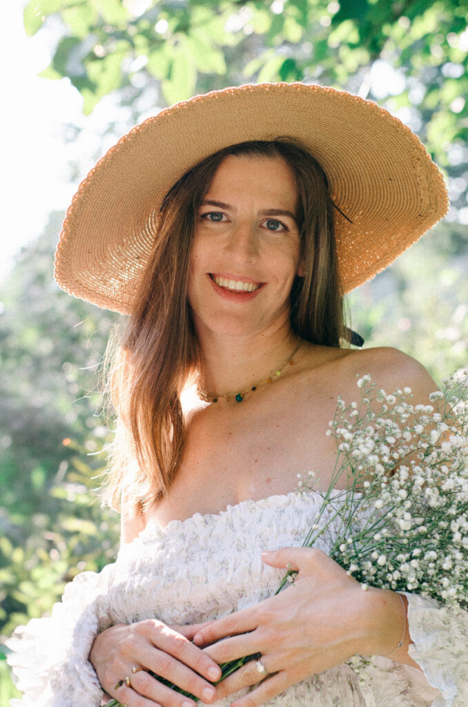 Cottage-core aesthetic of a pregnant woman in a white cotton dress and a round straw hat holding baby's breath flowers.