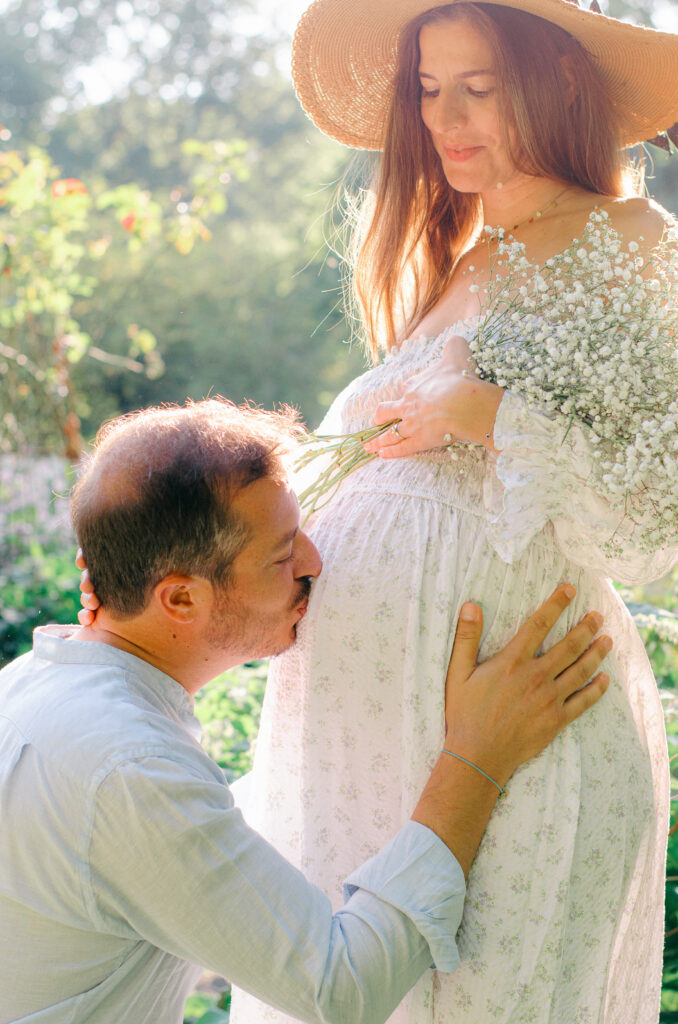 Husband bends down to kiss wife's baby bump in the Miracle Garden.