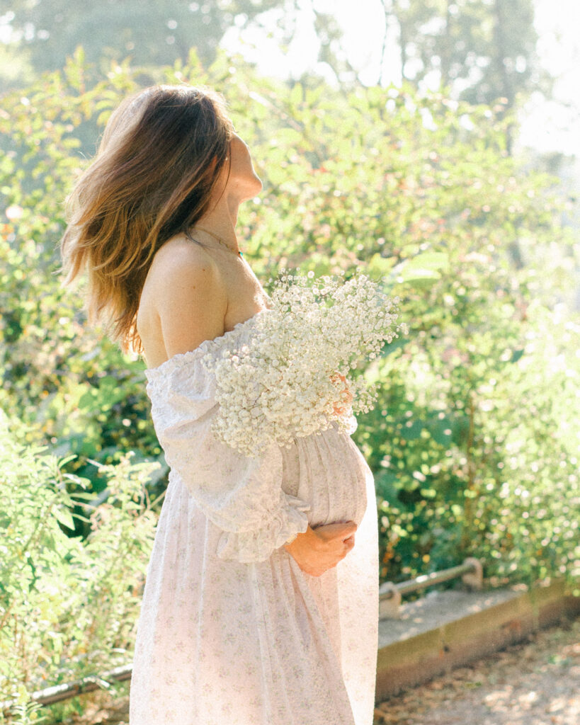 Expecting mother shakes her hair out, surrounded by blooms.