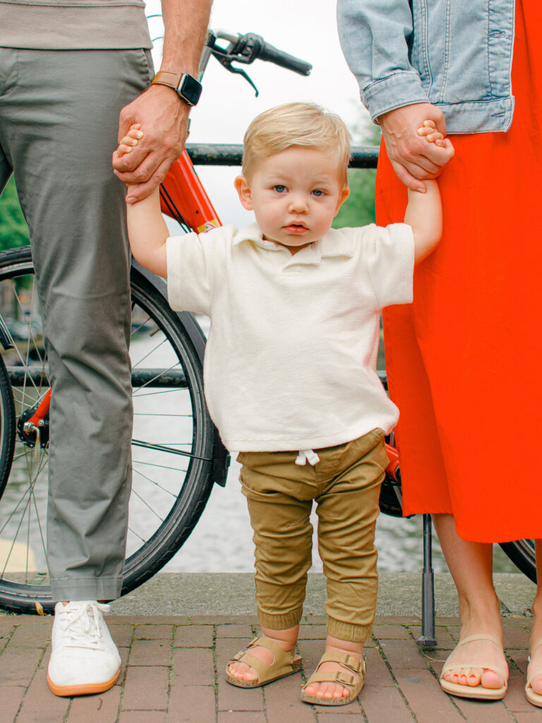 A toddler boy holds his parent's hands on a bridge in the Nine Streets.
