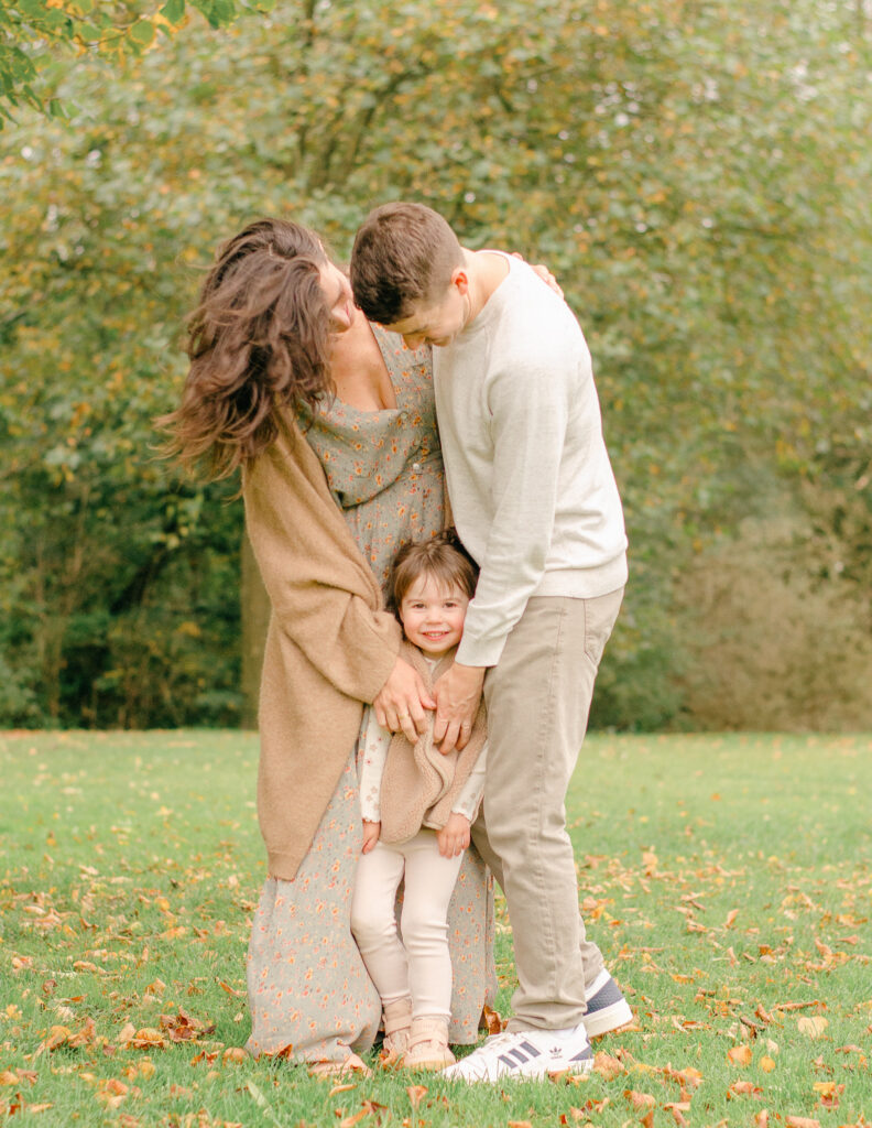 Parents holding child under a tree during cozy autumn moment.