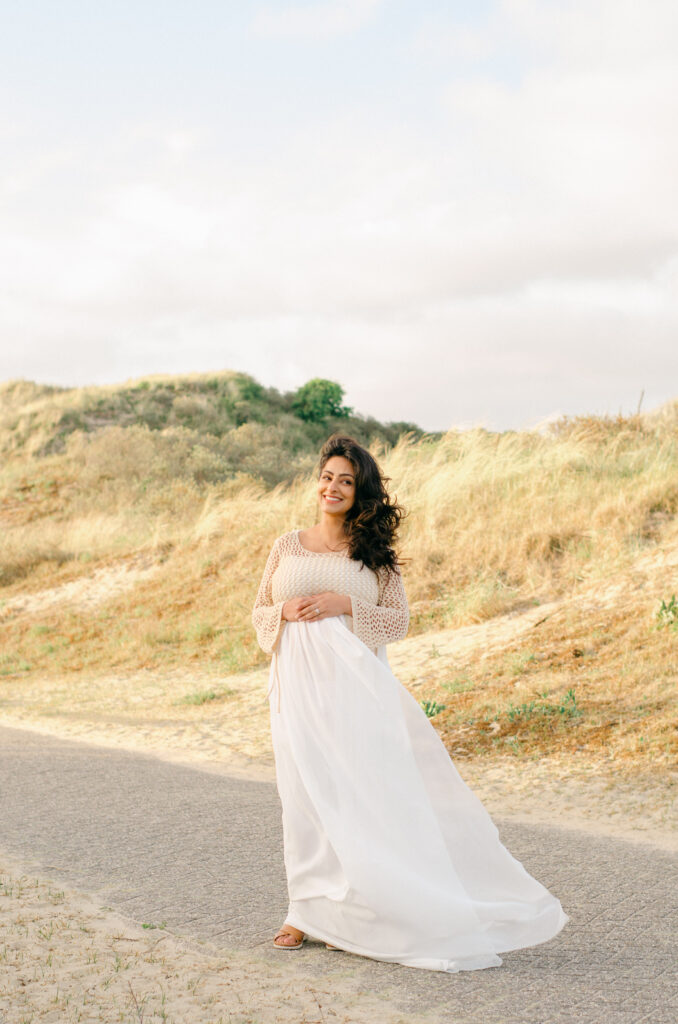 The wind sweeps the white flowy skirt of an expecting mama at sunset.