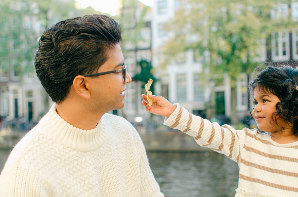 Toddler shows her father a leaf with the Amsterdam Canal houses behind them.