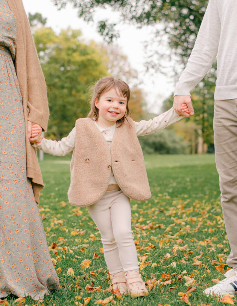 Toddler swings between her parents during a cozy autumn moment.