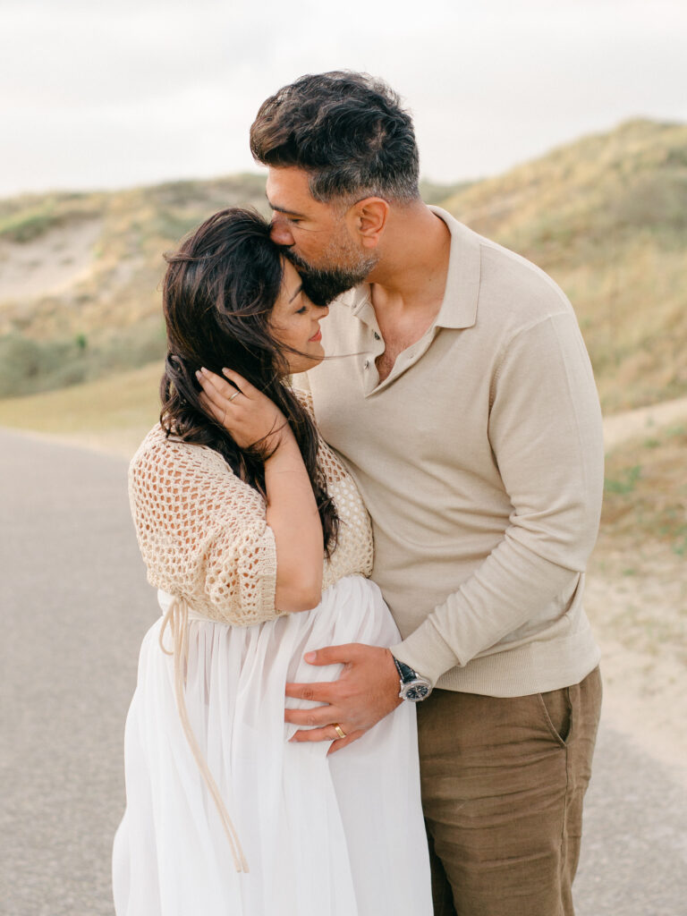 Husband kisses expecting wife on the forehead and cradles her bump.