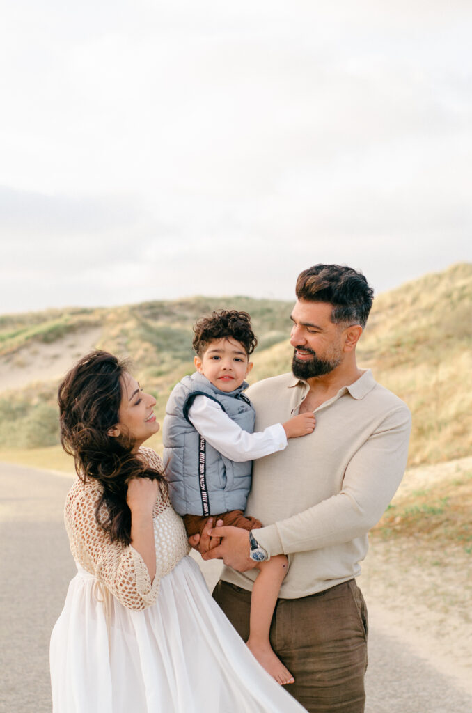 An expecting couple laugh with their toddler son in the Bloemendaal dunes.