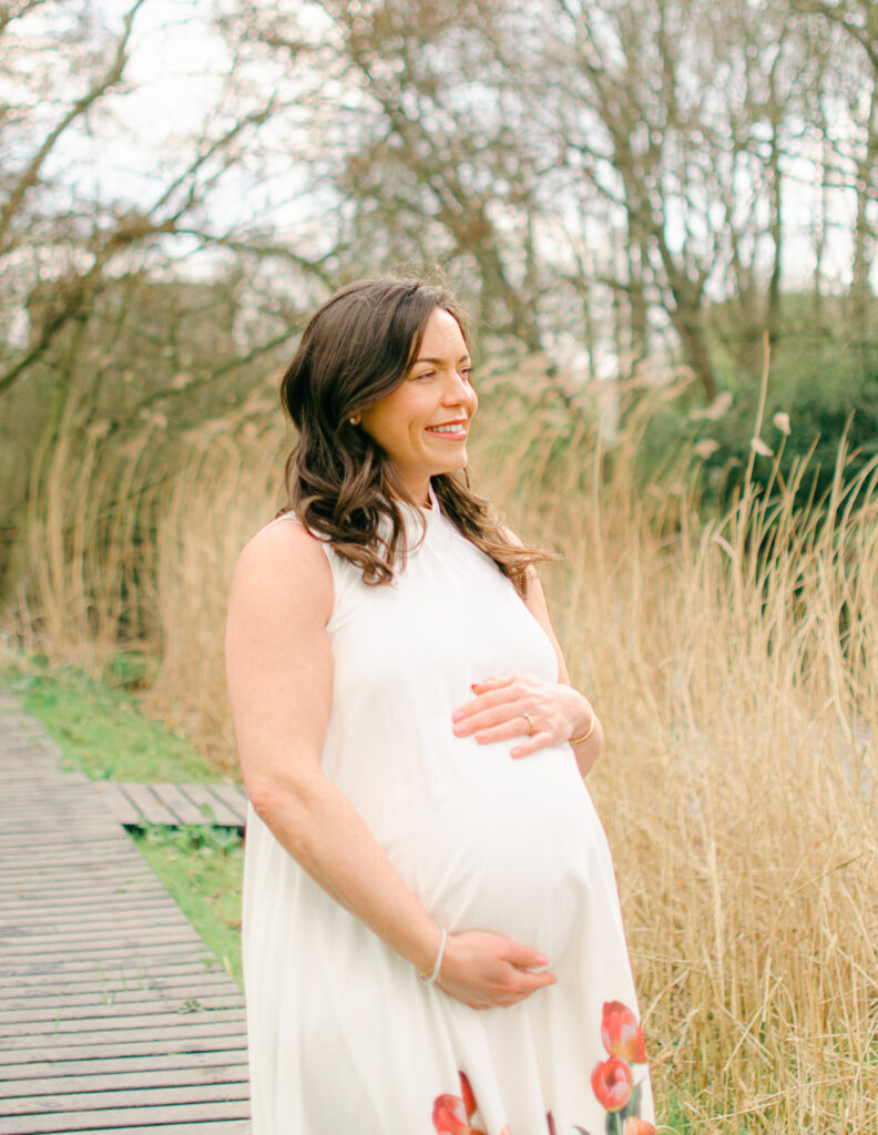 "Pregnant woman in white dress walking through Erasmuspark with blooming trees in the background"