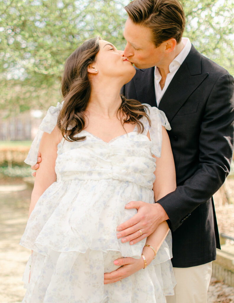 "Backlit photo of maternity couple embracing with golden light filtering through trees"