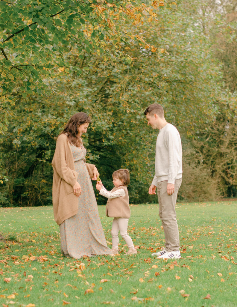 Daughter brings fall leaves to put in her mother's pocket during a family session.