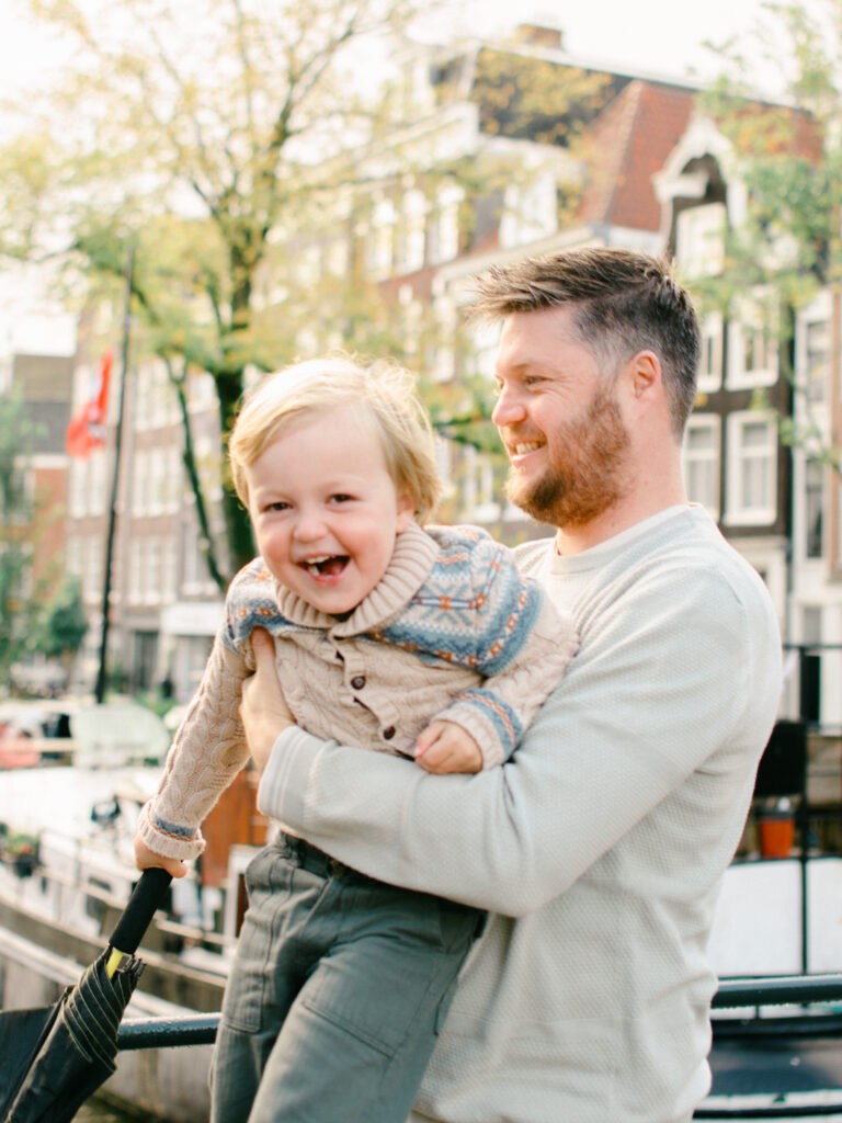 Lifestyle image of dad swinging little boy around in the Jordaan district, with the sun behind them.