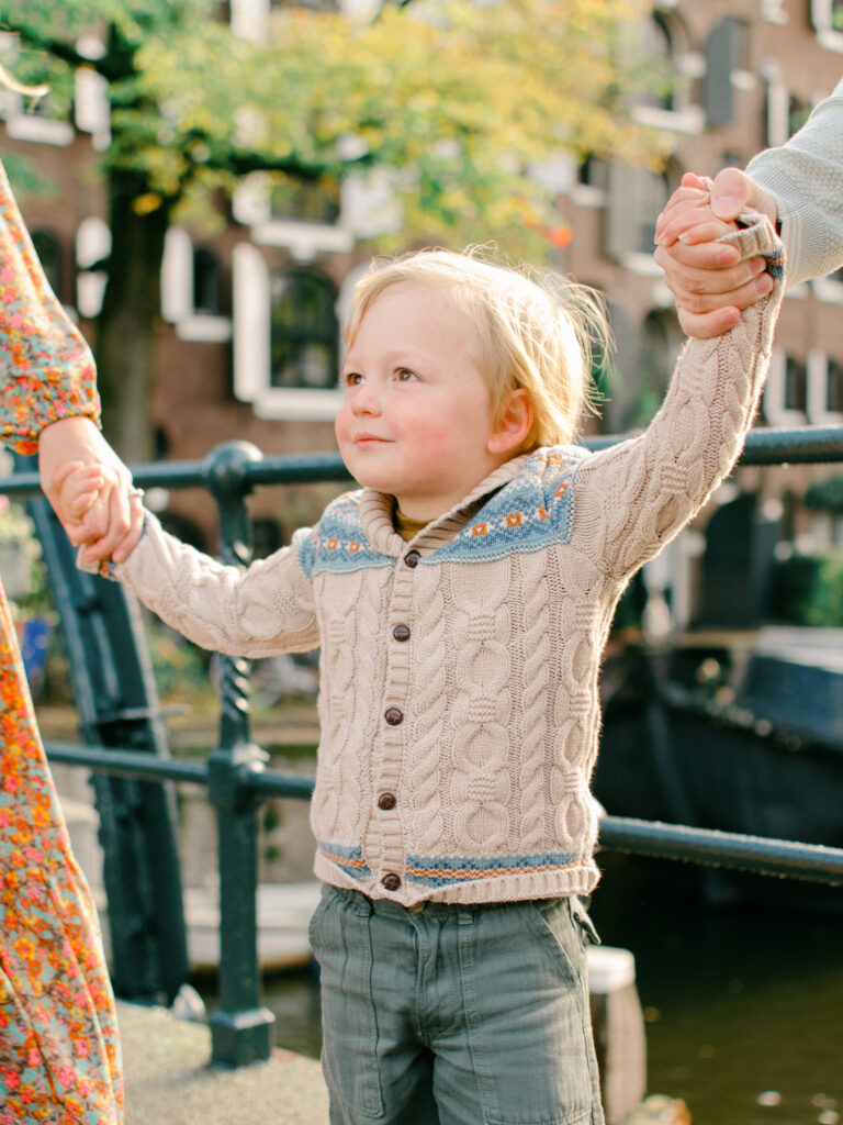 Little boy holds his parents hands walking across a bridge in Jordaan.
