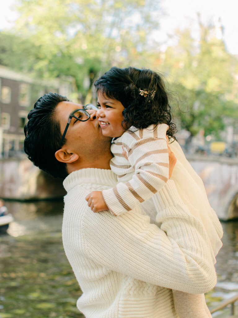 Dad gives his daughter a snuggly kiss on the Keizersgracht canal, fall leaves and town houses in the background.