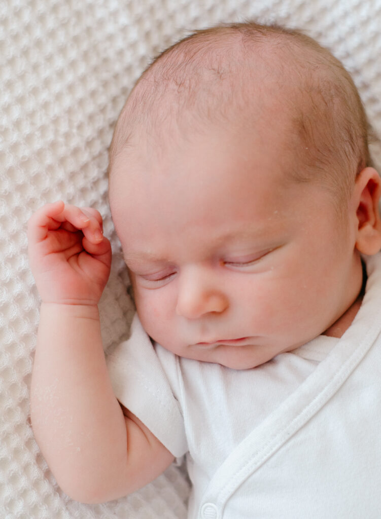 Softly sleeping baby on textured white blanket.