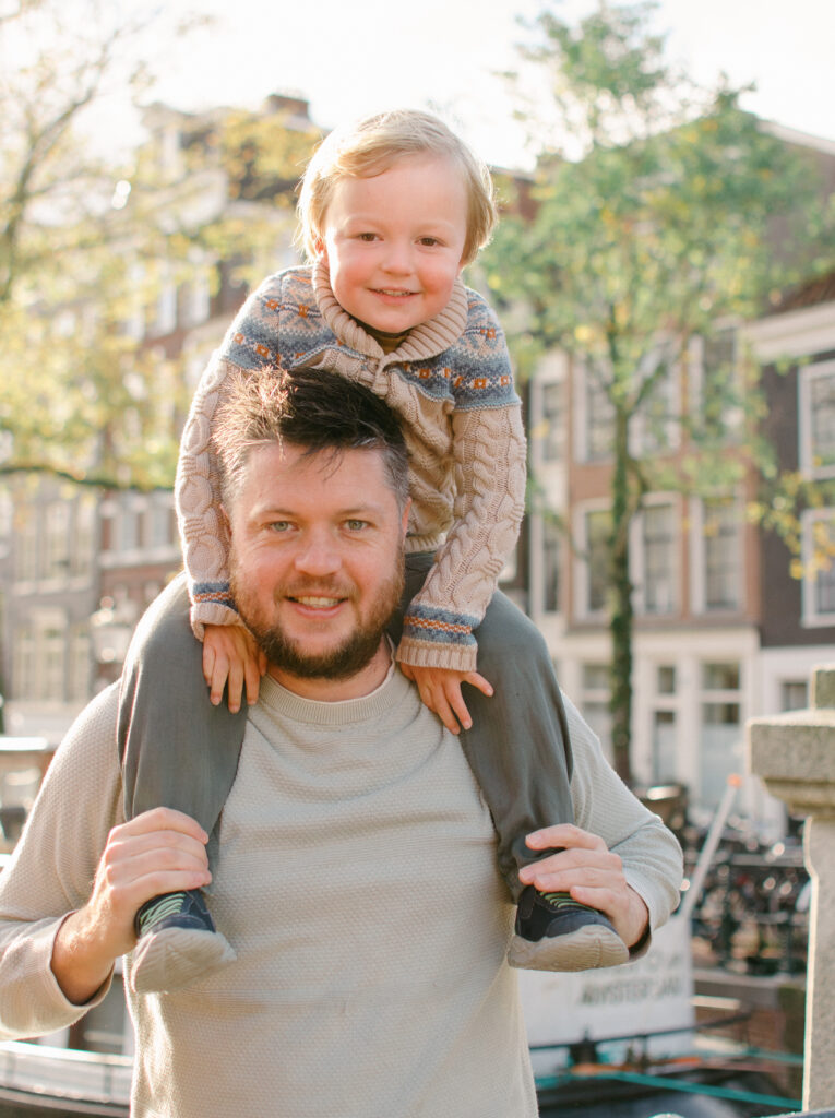 Dad carries son on his shoulders near an Amsterdam canal.