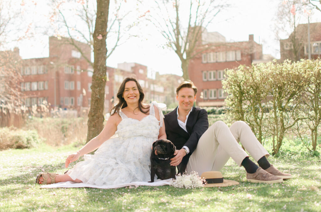 expecting couple sits on the ground near the canal in Erasmuspark.