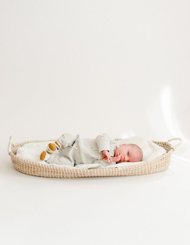 Newborn sleeping soundly in a bassinet on a white paper background.