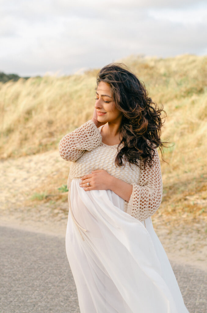 The wind sweeps an expecting mother's dress in the sand dunes near the beach.