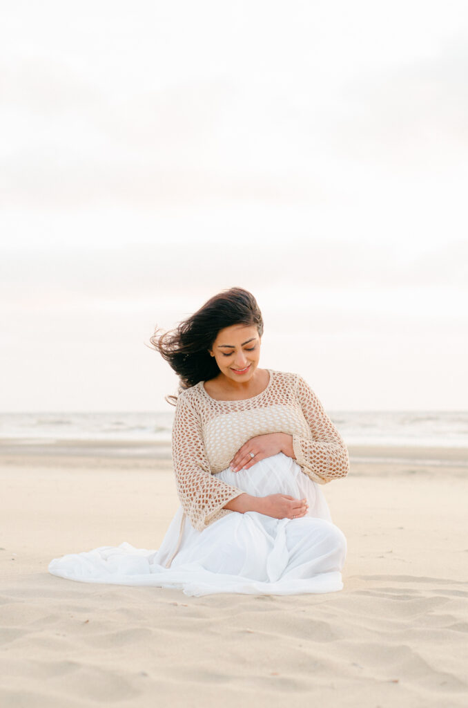 Wind catches an expecting mother's hair as she sits in the sand in Bloemendaal.