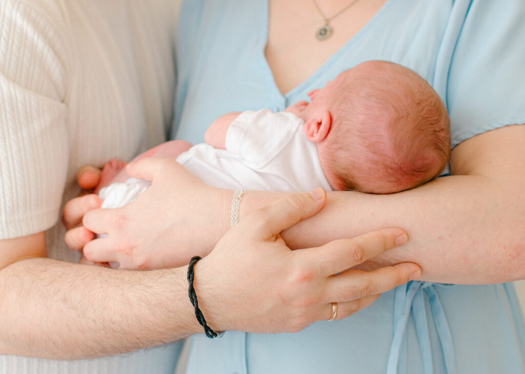 Parents cradle newborn wearing a white onesie.
