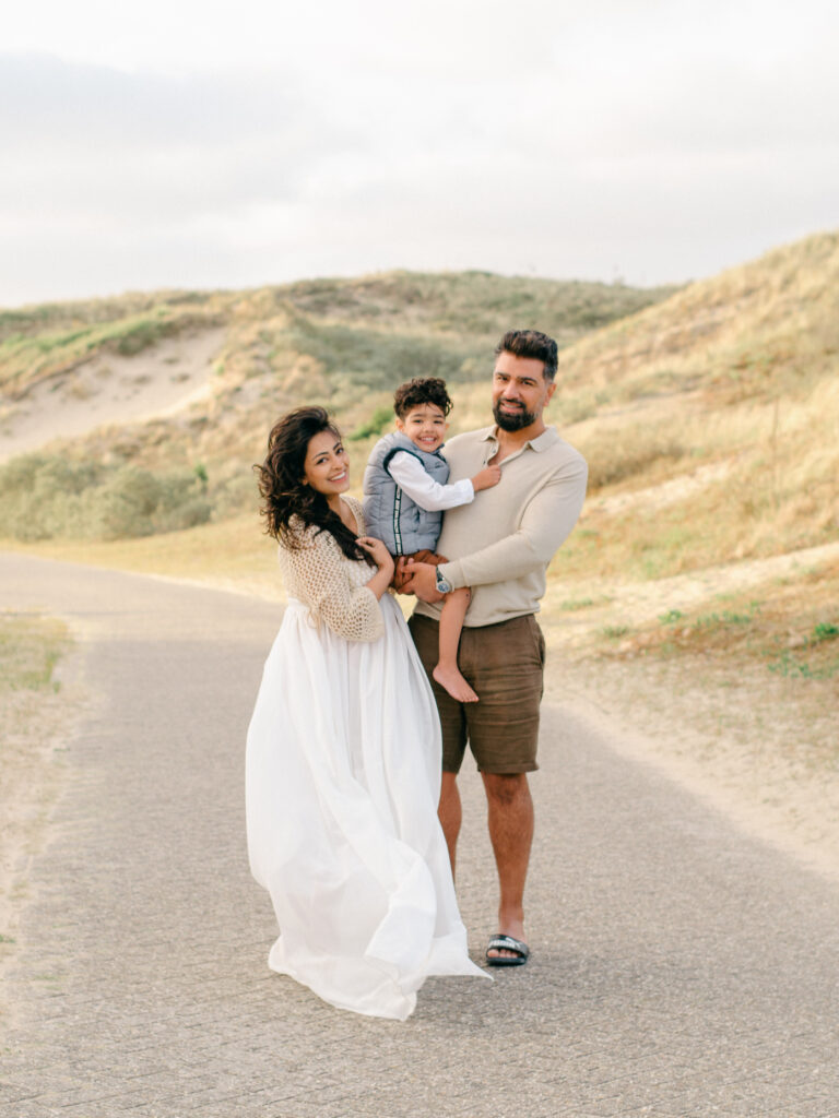 A family of three embrace in the dunes near the beach. 